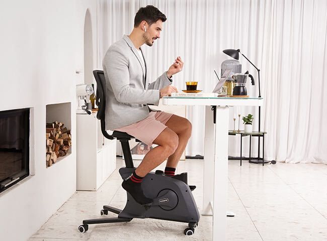 En man använder en motionscykel vid ett skrivbord under ett videomöte.